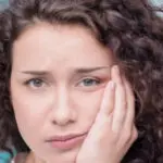 young woman holds her jaw in pain from emerging wisdom teeth