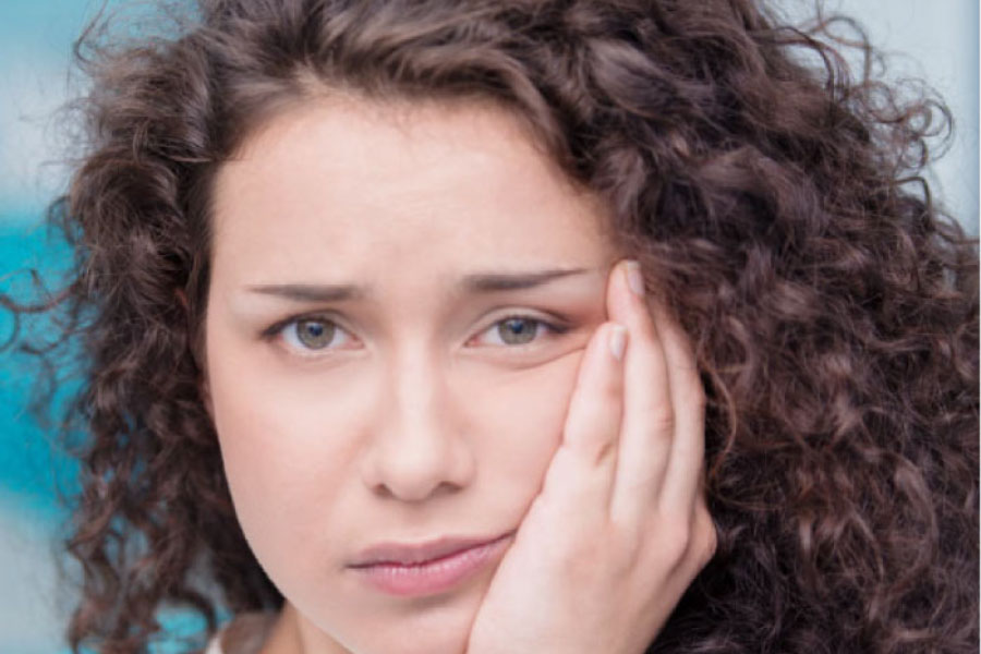 young woman holds her jaw in pain from emerging wisdom teeth